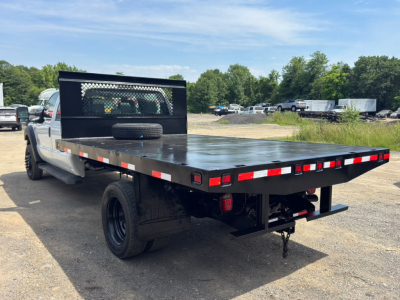 Flatbed tow truck with a black steel flatbed, rear view shows taillights, spare tire on bed, and a hitch; no visible branding text.