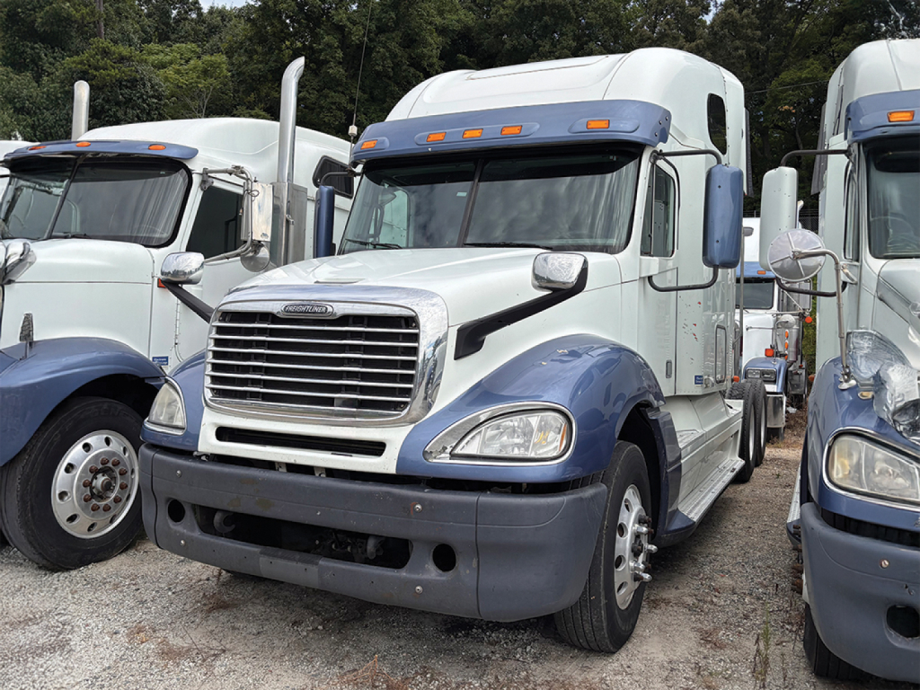 Freightliner CL120 Columbia sleeper truck in a used lot, front view with chrome grille, blue fenders, and white cab.