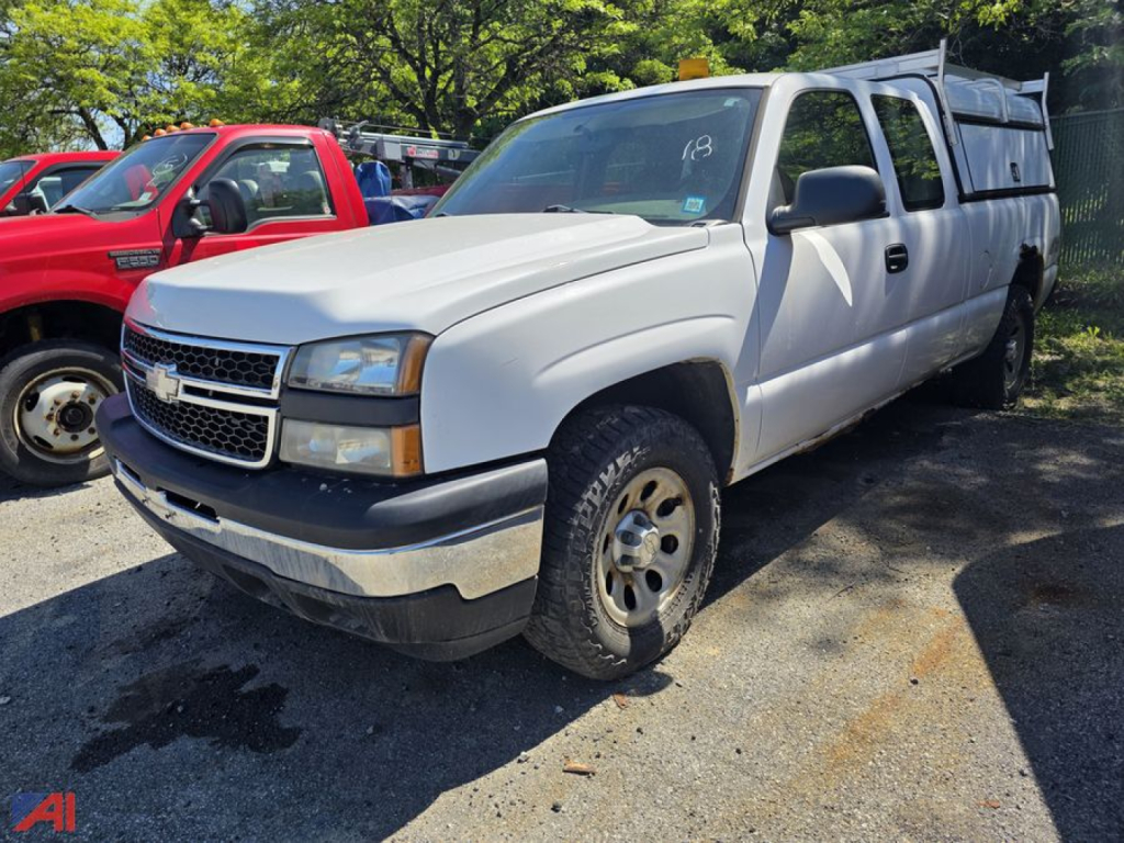 Chevrolet Silverado 1500 pickup with utility cap in a used vehicle lot, front-left view showing white body, extended cab, and cap on bed.