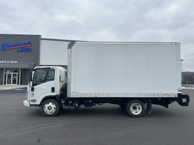 Truck side view with box body, front cab shows Hino styling; no visible text on box, dealership building in background.