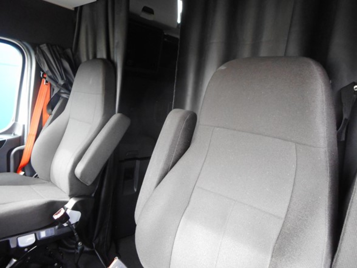 Cab area of a Freightliner Cascadia 126 truck showing seats and partition curtain.