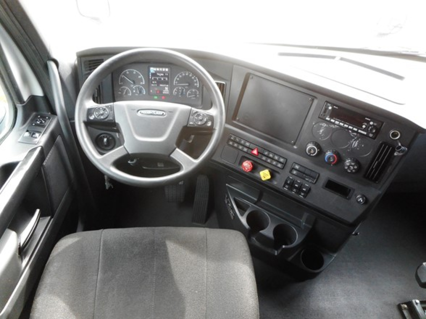 Cab interior of a 2023 Freightliner Cascadia 126 showing steering wheel, dashboard, gauges, large central display, and control panel.