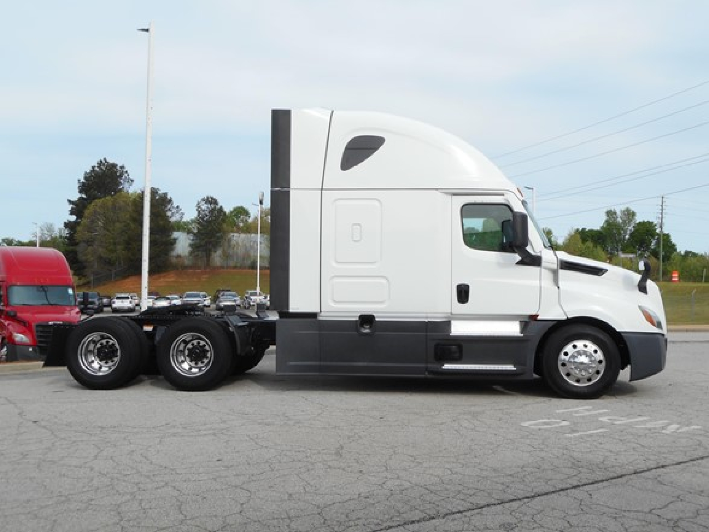 Truck chassis and cab of 2023 Freightliner Cascadia 126 viewed in profile with sleeper cab, three axles at rear, white exterior, black undercarriage.