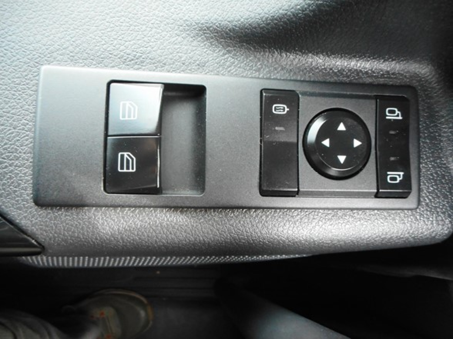 Dashboard window/mirror control panel with two window switch buttons and a circular directional pad on a textured surface.