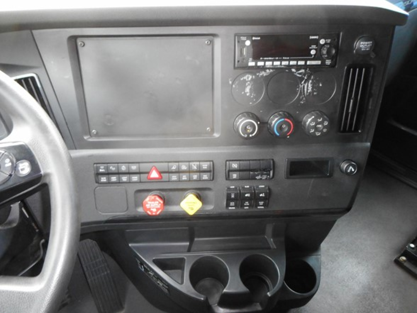 Cab interior of a 2023 Freightliner Cascadia 126 truck showing dashboard controls, circular gauges, vents, cup holders, and radio. Text visible on controls includes hazard button, various switches, and cup holders.