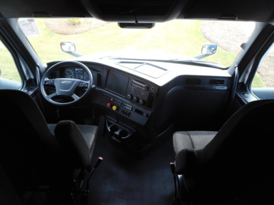 Interior of Freightliner Cascadia 126 cab showing steering wheel, dashboard with instrument cluster, center console controls, and passenger seat.