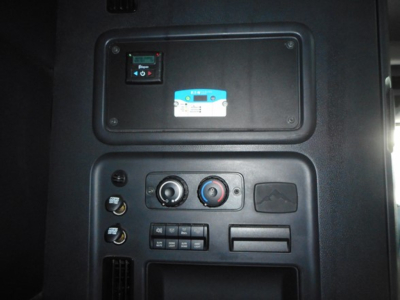 In-cab view of a Freightliner Cascadia dashboard with controls and a small blue-and-white sticker panel.