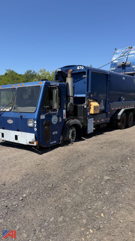 Crane Carrier garbage truck side-view showing blue body with compactor and arm, 470 number on cab, debris container, and side loader mechanism.