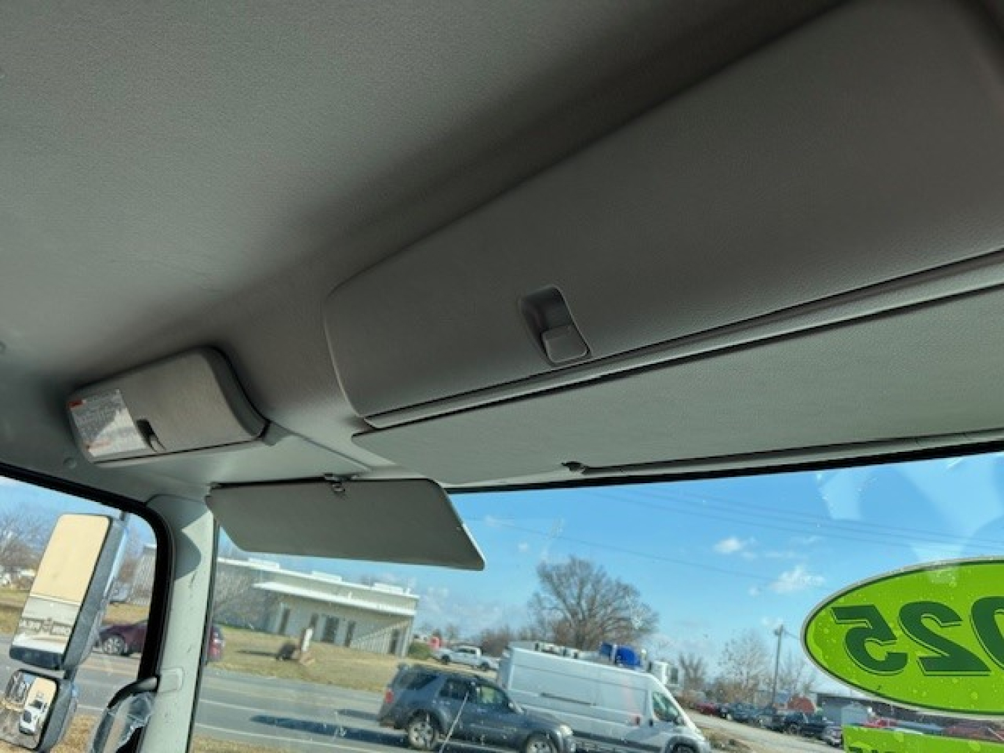 Cab interior showing sun visor and windshield with green 315 sticker; dashboard area and rear view mirror; outside view includes a blue sky and a white van.