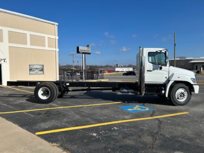 Truck cab and chassis on a lot, white cab, long flatbed frame, front view with wheel hubs, parking lines visible.