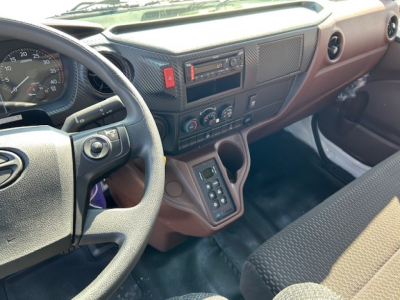 Cab and chassis interior showing steering wheel, dashboard, center console with control buttons, gear selector panels, and brown upholstery in a 2025 Hino L7.