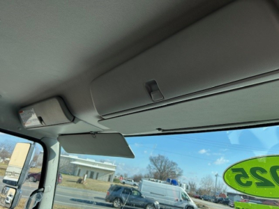 Cab interior showing sun visor and windshield with green 315 sticker; dashboard area and rear view mirror; outside view includes a blue sky and a white van.