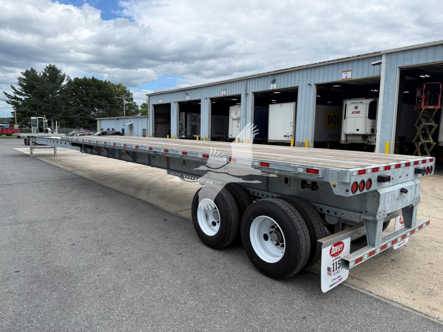 Flatbed trailer with extendable centerbeam showing diamond plate deck and dual rear axles in a yard.