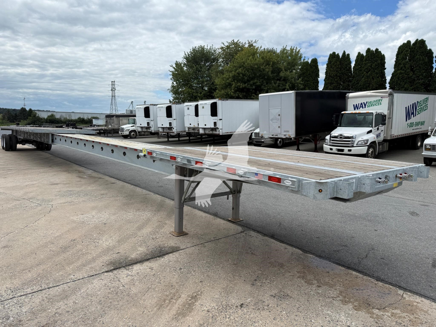 Extendable flatbed trailer with extendable deck and white cab overheating in yard. VIN 7KYEF4821VED49031 stock VED49031 Way intermodal trailers in background.