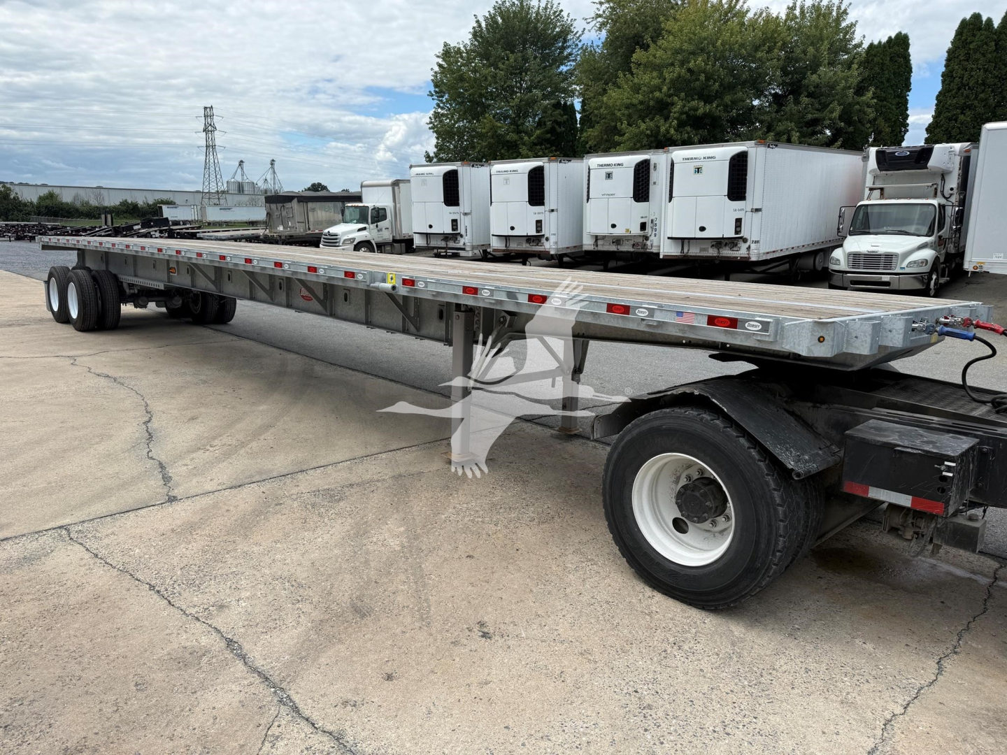 Extendable flatbed trailer showing long aluminum deck with multiple axles and white cab-over containers in background.