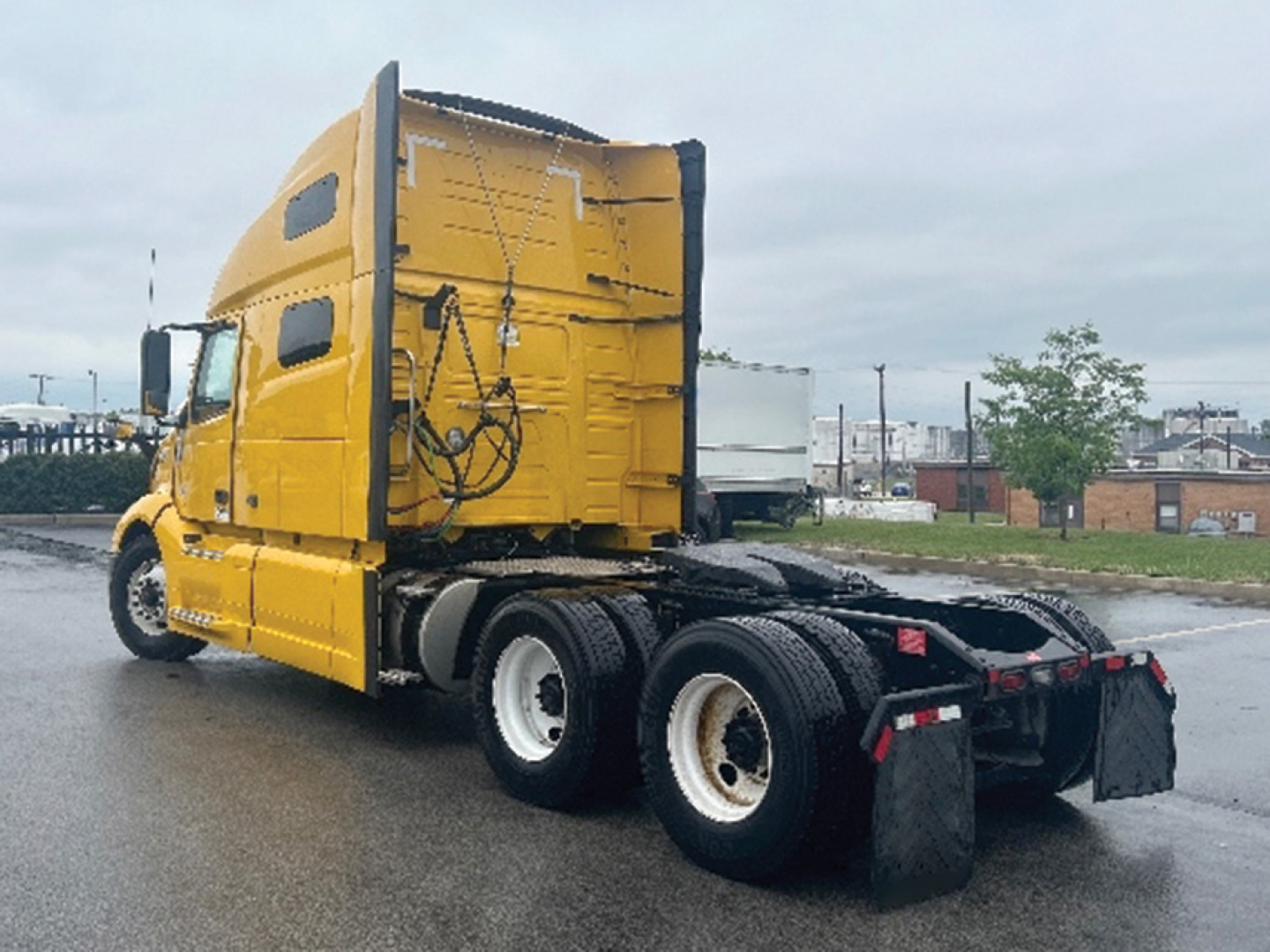 Volvo VNL 760 sleeper cab tractor in a yard showing rear and side with yellow paint, dual rear axles, and fifth wheel.