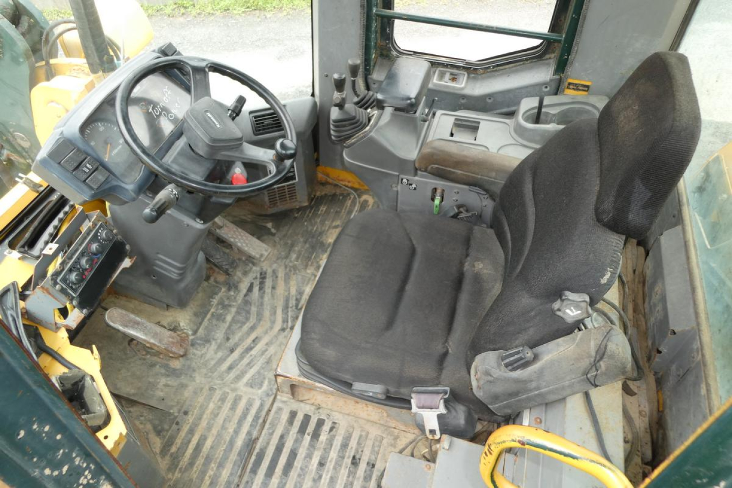 Interior of a Kawasaki 65TMV wheel loader cab showing steering wheel, control levers, and operator seat with floor mat.