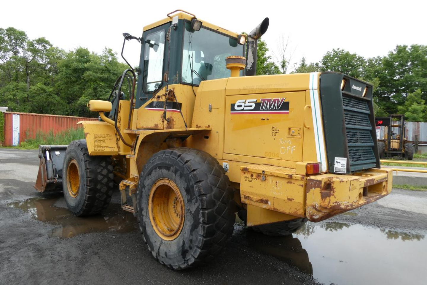 Kawasaki 65TMV wheel loader in-service showing side and rear with 65TMV decal on door and heavy tires.