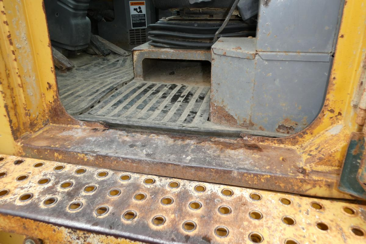 Kawasaki 65TMV wheel loader cab entry with rusted metal step and perforated steel platform; interior floor and pedal area visible.