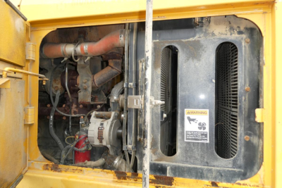 Kawasaki 65TMV wheel loader engine bay with visible hoses, alternator, and radiator area; yellow casing and warning label.