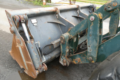 Backhoe loader breakout bucket attachment on Kawasaki 65TMV wheel loader showing hydraulic pins and wear bars.