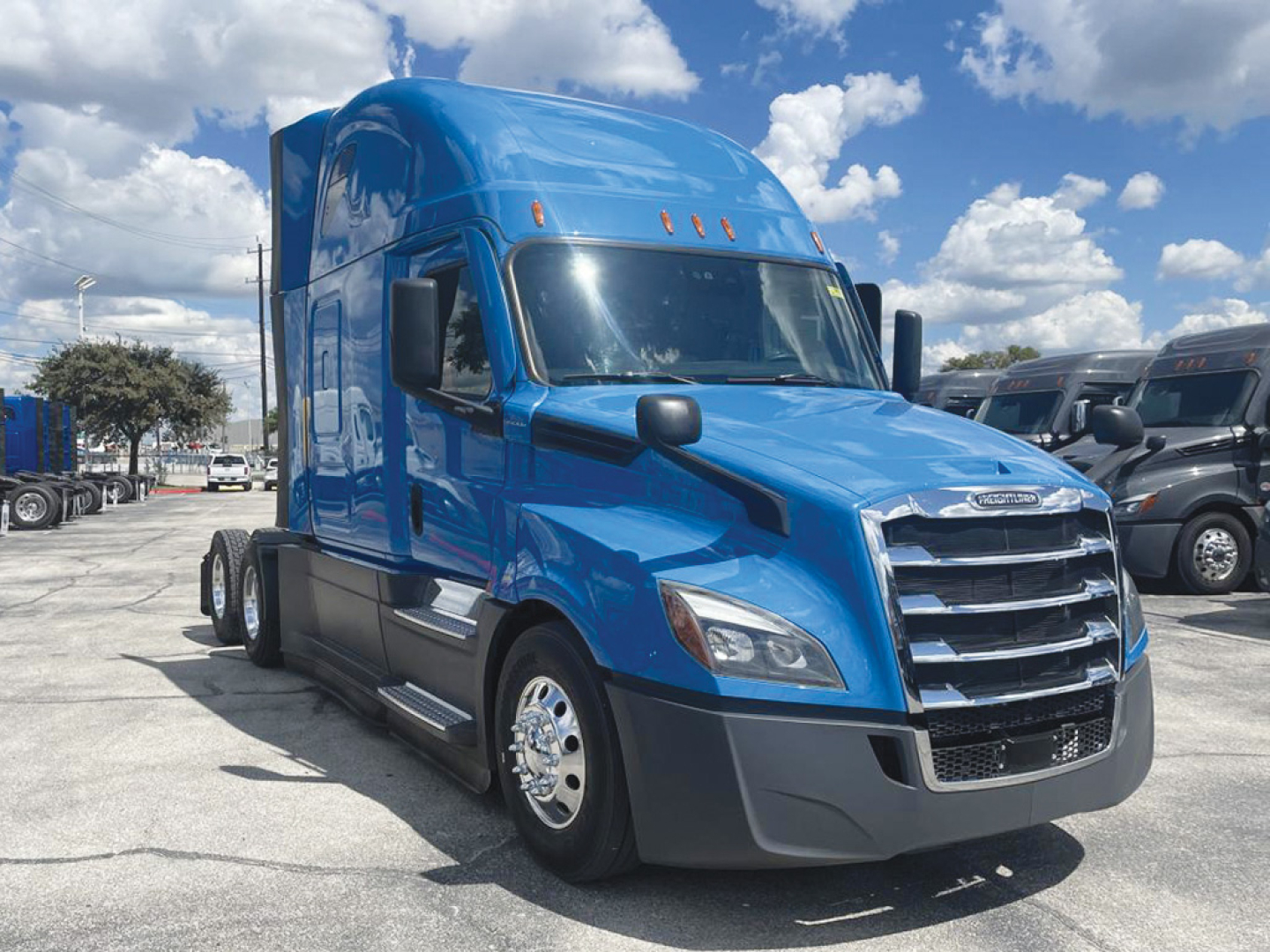 Blue 2022 Freightliner Cascadia126 tractor in a parking lot, front-left view showing grille, chrome wheels, side steps, and sleeper cab.