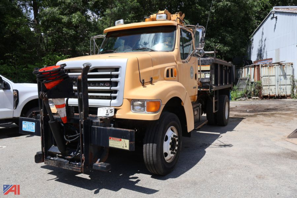 Dump truck front-left view showing 2001 Sterling L8500 Series with front-mounted snowplow/attachment and amber cab, yellow body, dump bed visible.