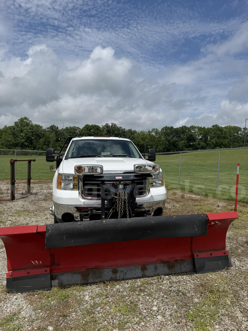 Truck with front plow attachment—2009 GMC Sierra 3500HD visible head-on with diesel grille guard and red snow plow in foreground.