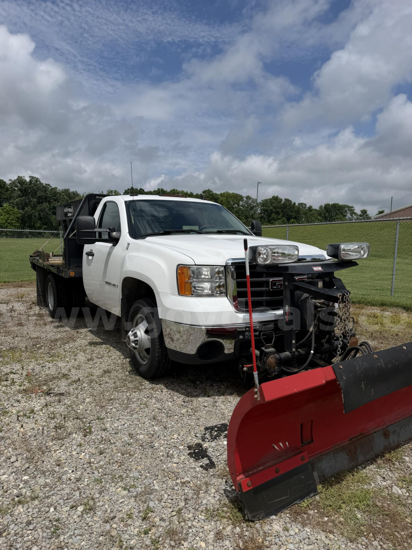 Trucks showing 2009 GMC Sierra 3500HD with plow attachment in front, white cab, dual exhaust, warning lights, and off-road tires.