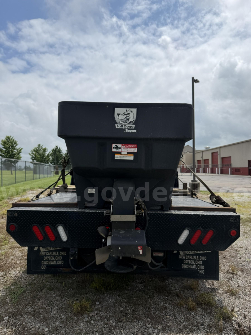 Back of GMC Sierra 3500HD utility/plow truck showing rear bumper with lights and a dump bed tailgate. Text on bumper and warning labels visible.