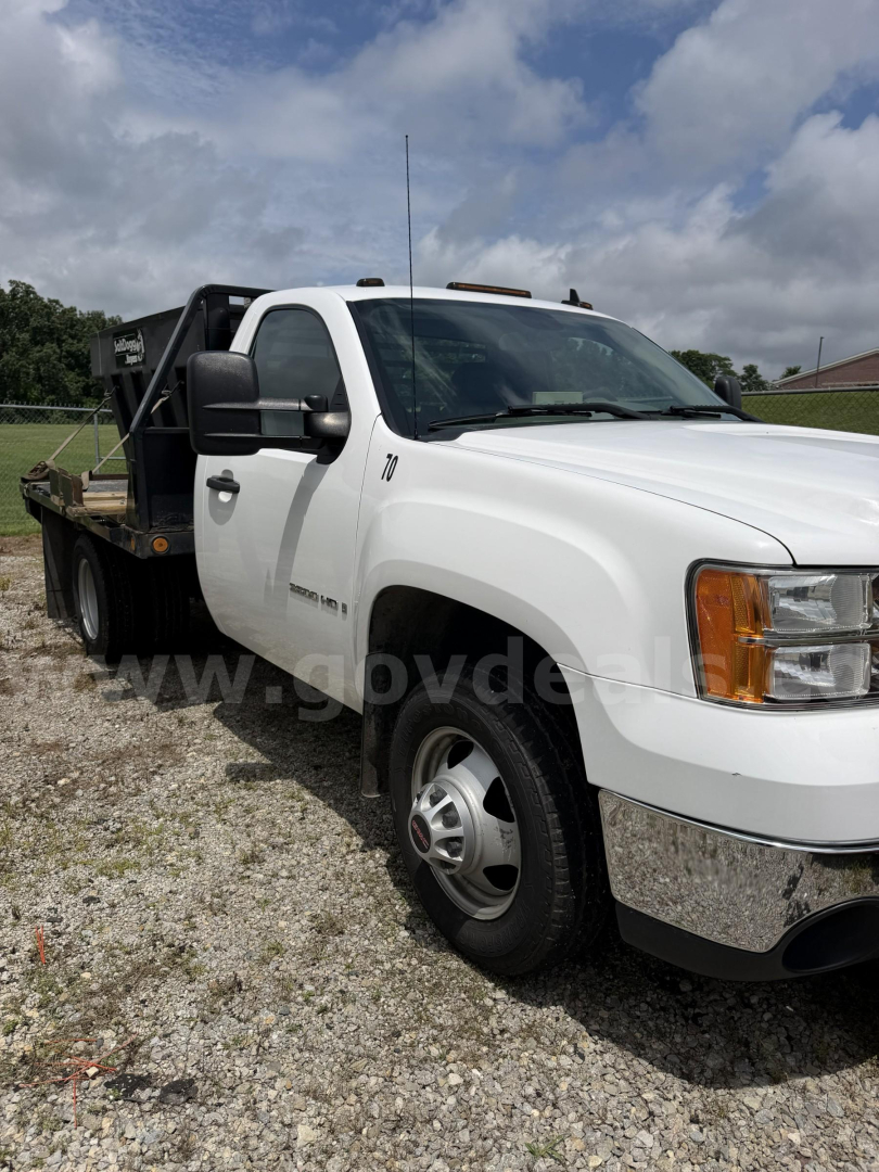 GMC Sierra 3500HD side view showing plow-ready heavy-duty truck with white cab and black flatbed in gravel lot.