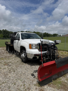 Trucks showing 2009 GMC Sierra 3500HD with plow attachment in front, white cab, dual exhaust, warning lights, and off-road tires.