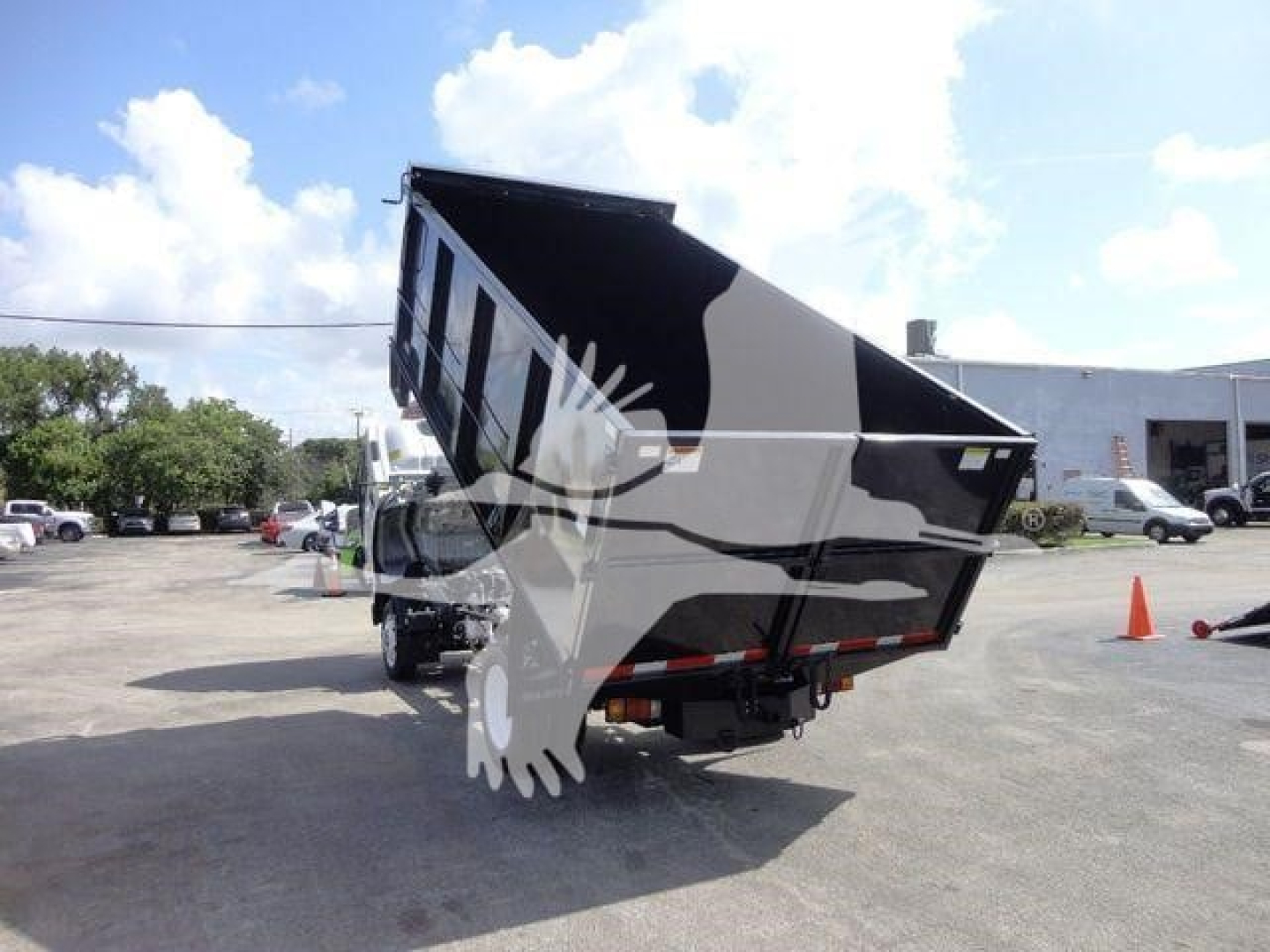 Dump truck with raised bed showing Isuzu NPR oversized dump body. Visible branding on side panels and hydraulic mechanism under bed.