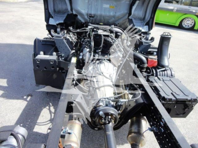 Isuzu NPR-HD truck engine bay view with open hood showing multiple hoses, belts, and components; front chassis visible.