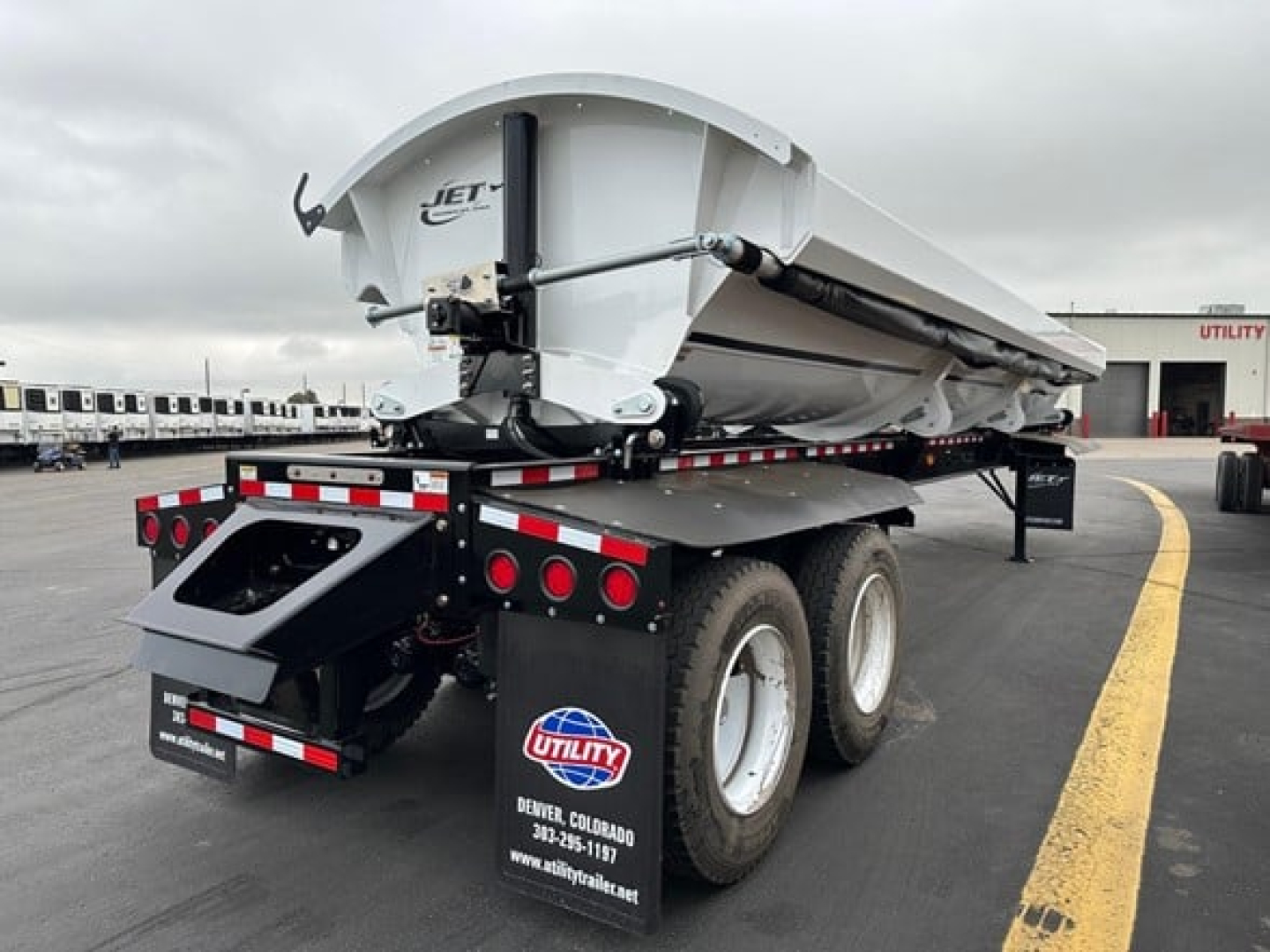 Jet side dump trailer showing rear view with white tank, dual rear axles, and Utility logo. Visible text: JET on the hopper, Utility branding on mudguard, wheels, and rear bumper.