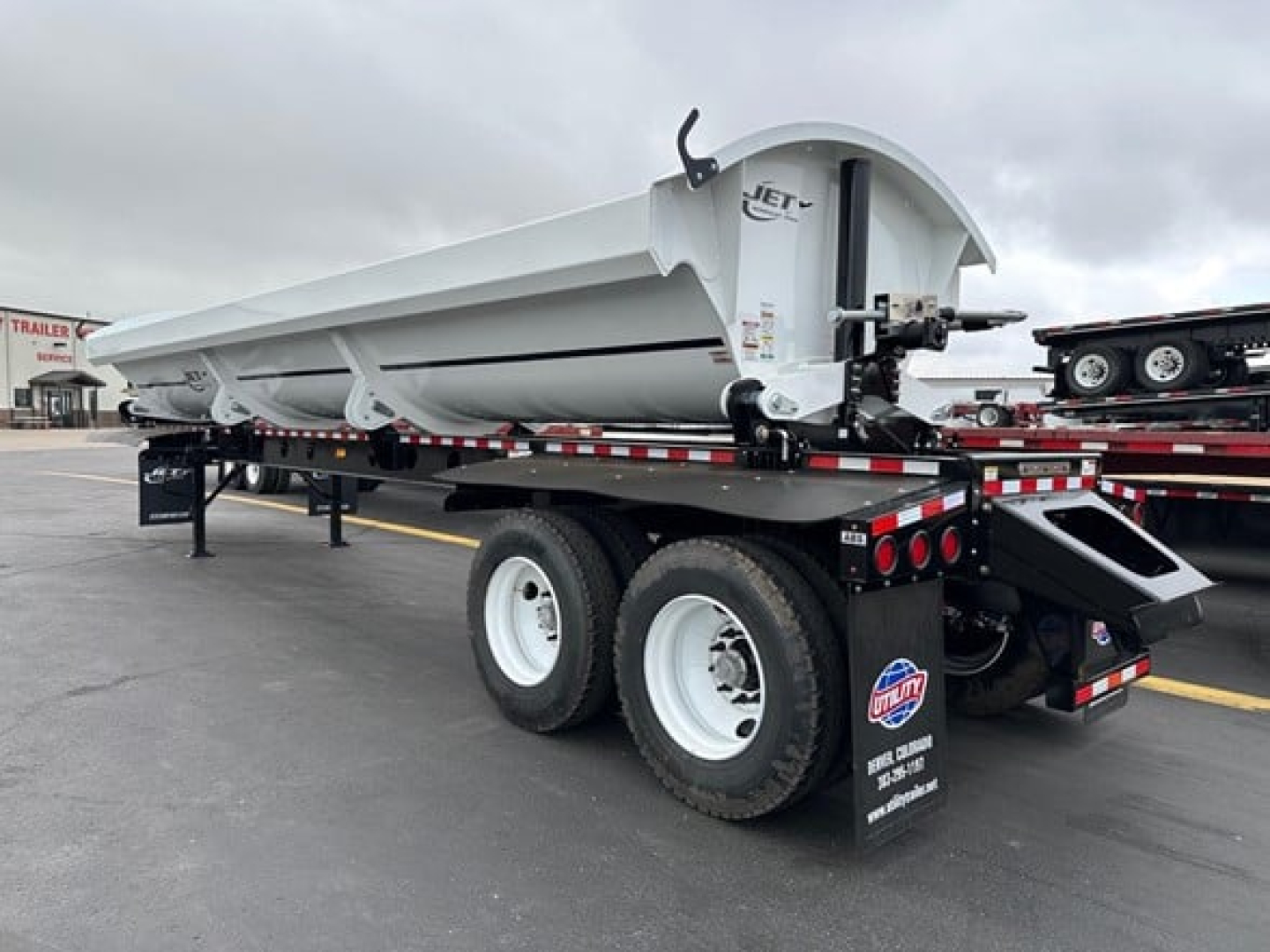 Jet side dump trailer showing tandem axle configuration and white painted wheels with a raised dump bed.