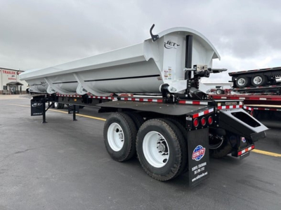 Jet side dump trailer showing painted white body and dual rear axles with black chassis and white rims, equipment label on front, rear ramp, and light setup.