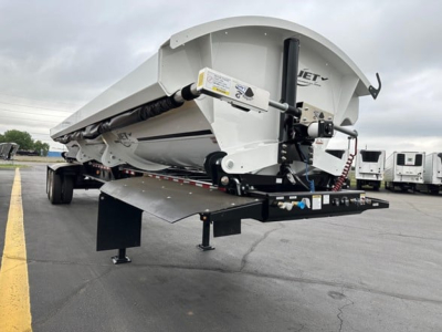 Jet side dump trailer folded on a trailer deck, white body with hydraulic cylinder and support legs visible; branding and safety decals on the side.