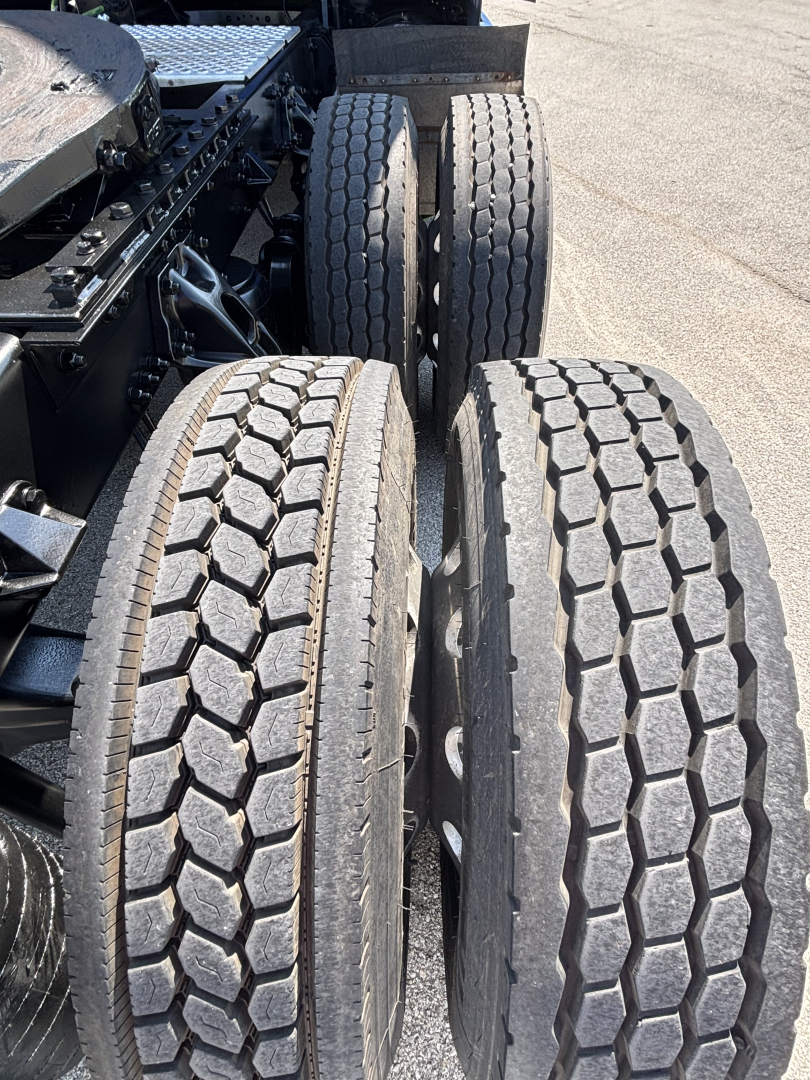 Tandem rear axle view of a Kenworth truck showing dual tires with tread pattern and wheel hubs.