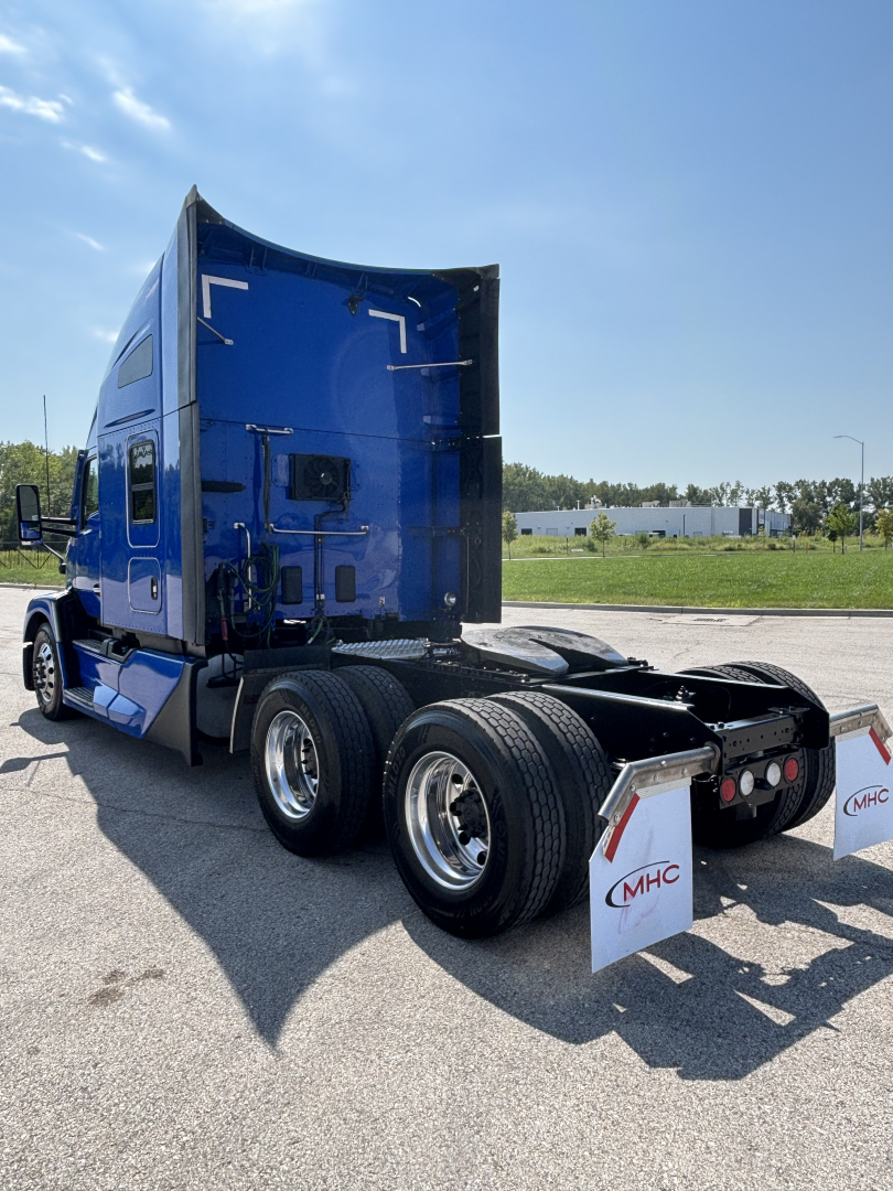 Kenworth T680 tractor rear angle showing blue sleeper cab and dual rear wheels with fenders and light setup.