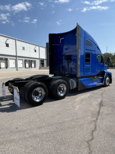 Kenworth T680 blue semi truck side rear view showing sleeper cab and rear wheels.
