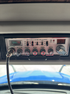 Kenworth T680 dashboard showing Cobra CB radio with labeled knobs and a digital display, mounted under the windshield.