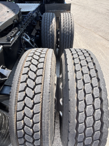 Tandem rear axle view of a Kenworth truck showing dual tires with tread pattern and wheel hubs.