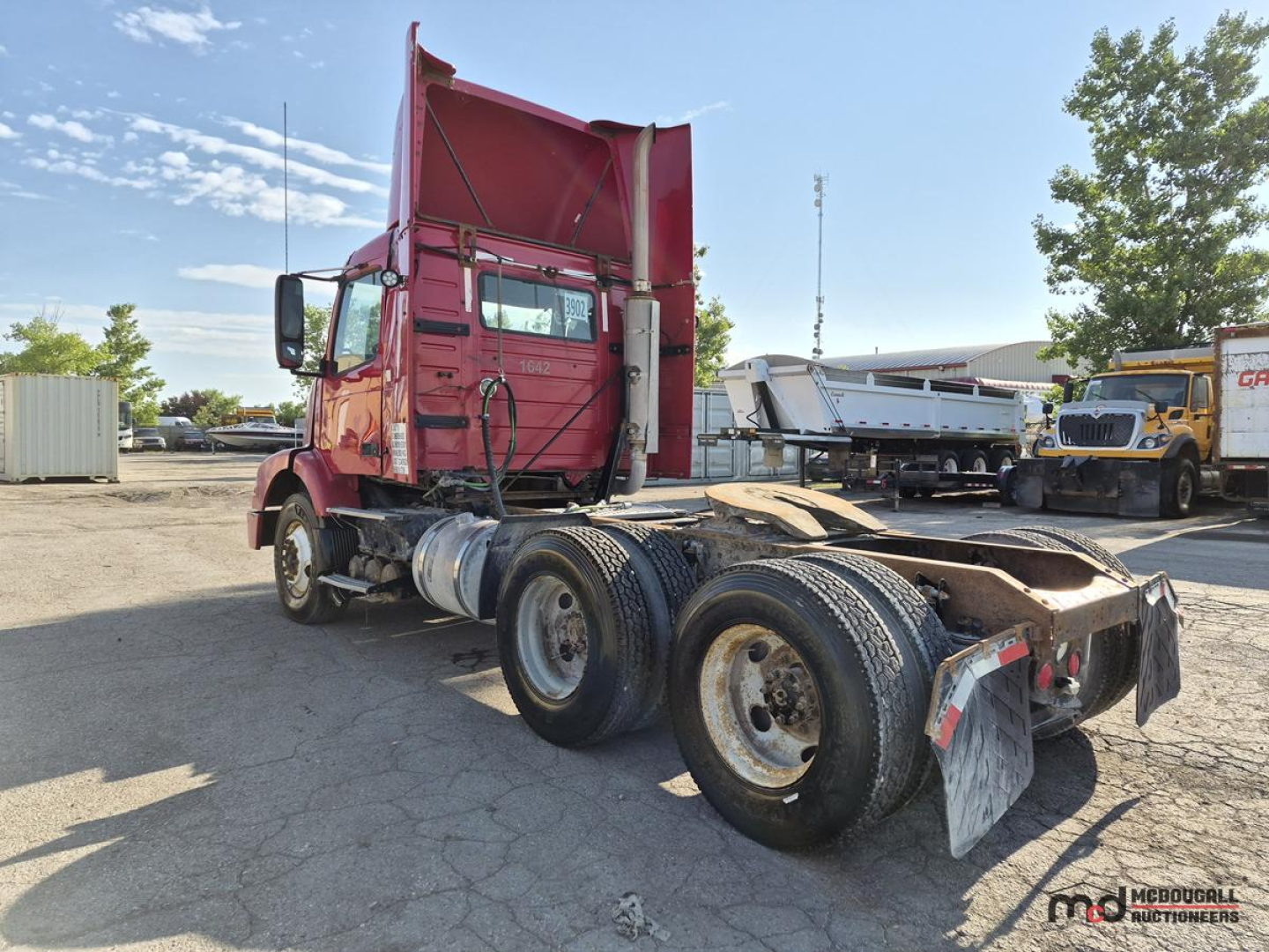 Truck chassis and cab of a red 2005 Volvo day cab tractor showing rear dual axles and fifth wheel with mud flaps and exposed driveline
