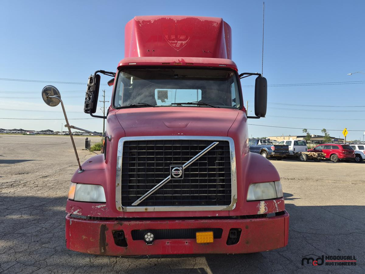 Front view of a red Volvo day cab semi truck with large grille, Volvo emblem, side mirrors, and windshield; visible wear on bumper.