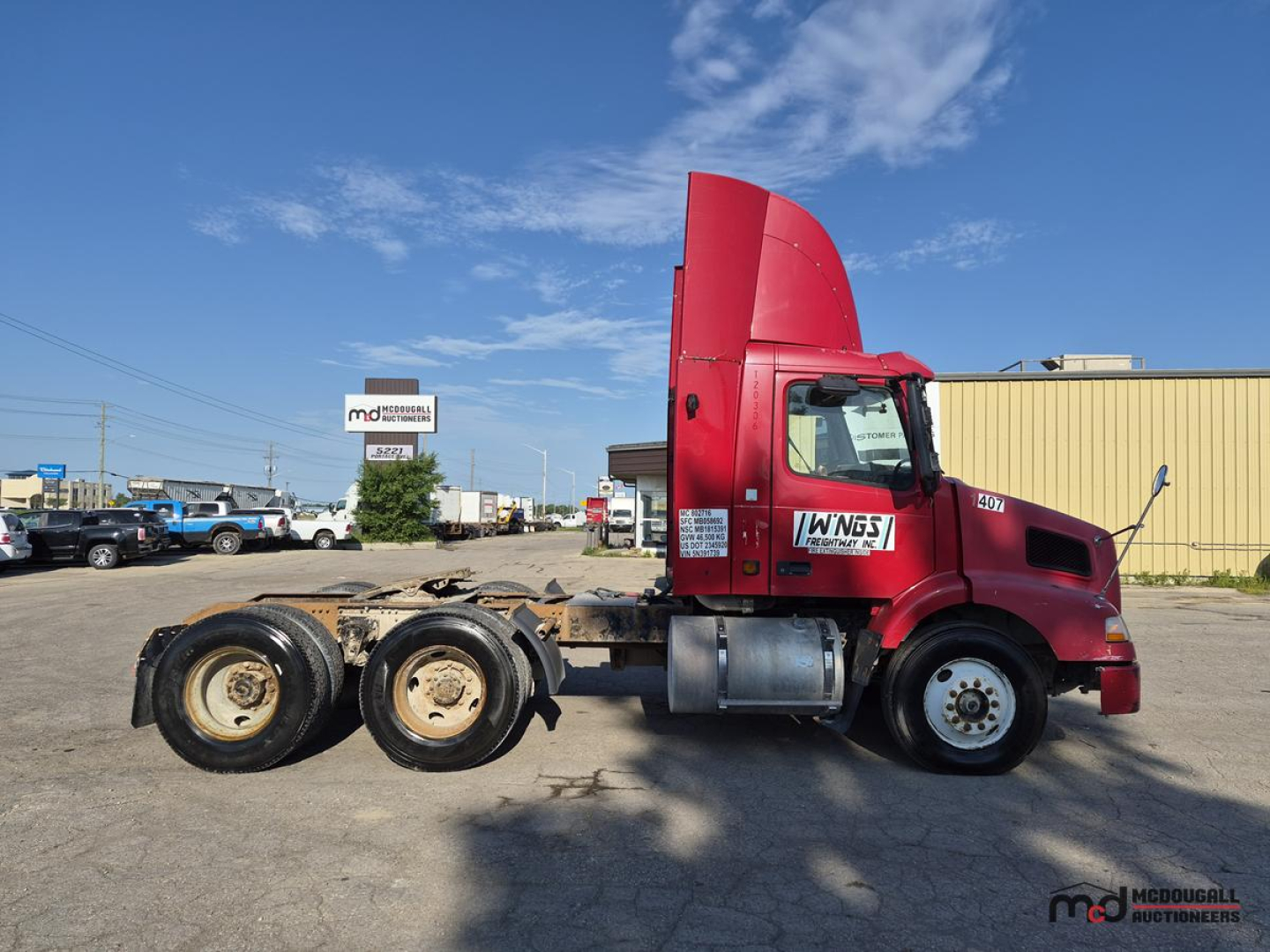 Volvo day cab tractor-trailer showing side view with red cab and rear dual rear axles, no trailer attached, blue sky background.