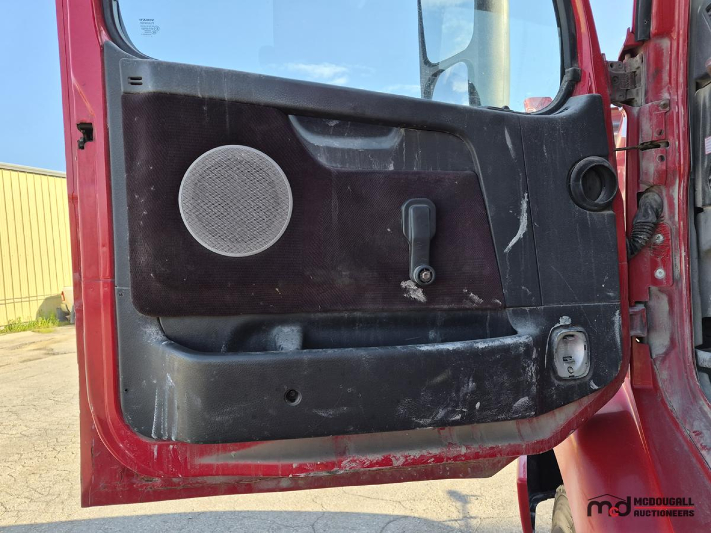 Door interior of a Volvo semi truck cabin showing a circular speaker, window crank, and door pocket with wear marks