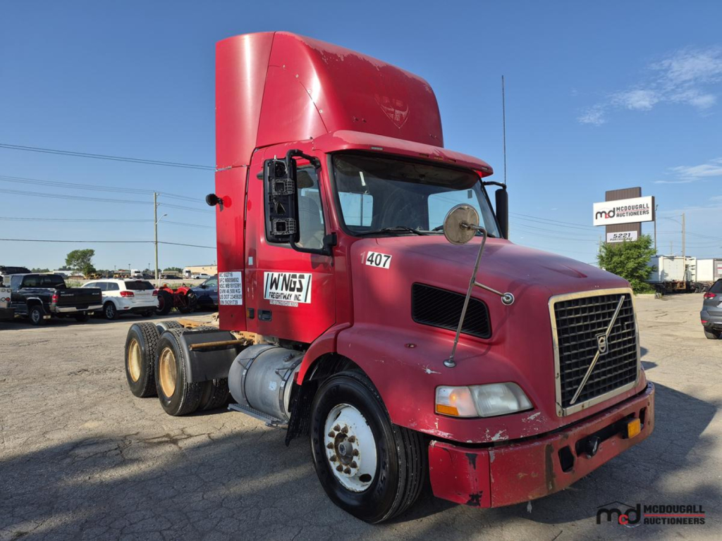 Volvo day cab semi truck, red exterior, front grille, cab with high sleeper, 6x4 tractor, used condition, VIN plate not visible, parked in lot with other trucks.