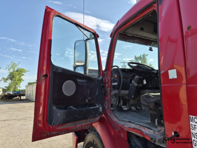 Truck cab interior visible through open driver door of a red 2005 Volvo day cab semi, showing dashboard, steering wheel, and worn floor mats.