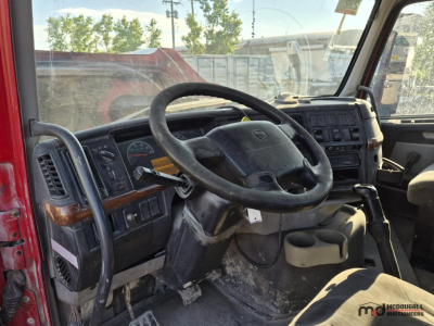 Volvo truck cockpit with steering wheel, dashboard, and gear shift showing interior controls and worn driver area.